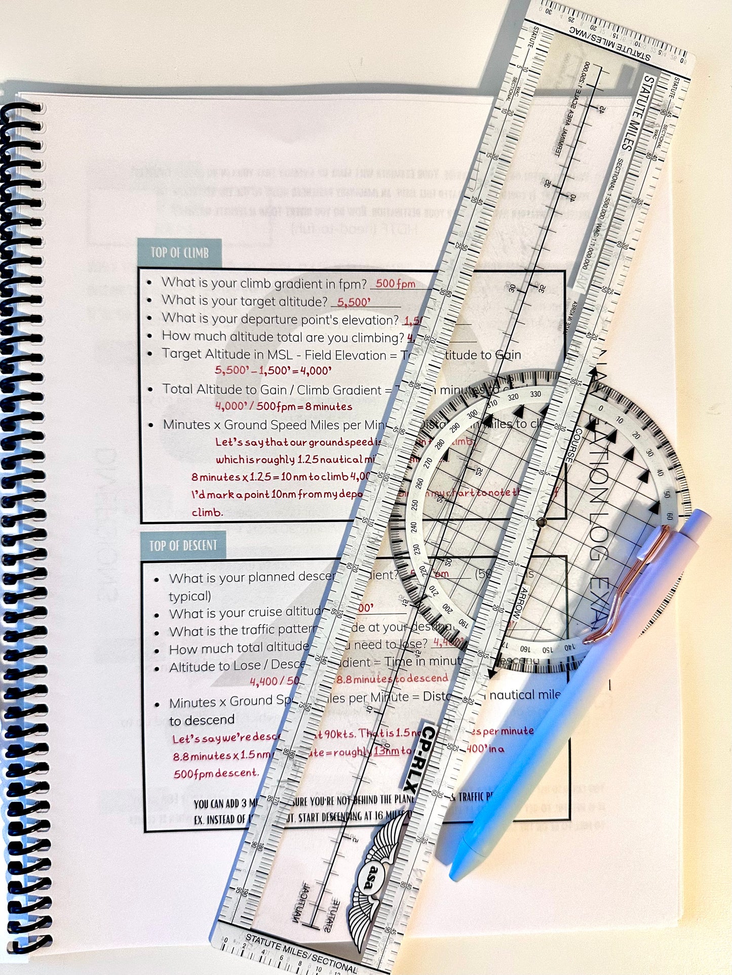 One of the pages of the aviator’s notebook. It is a navigation log example worksheet with a plotter on top and a pen. This page is meant to help student pilots plan their cross country flights.