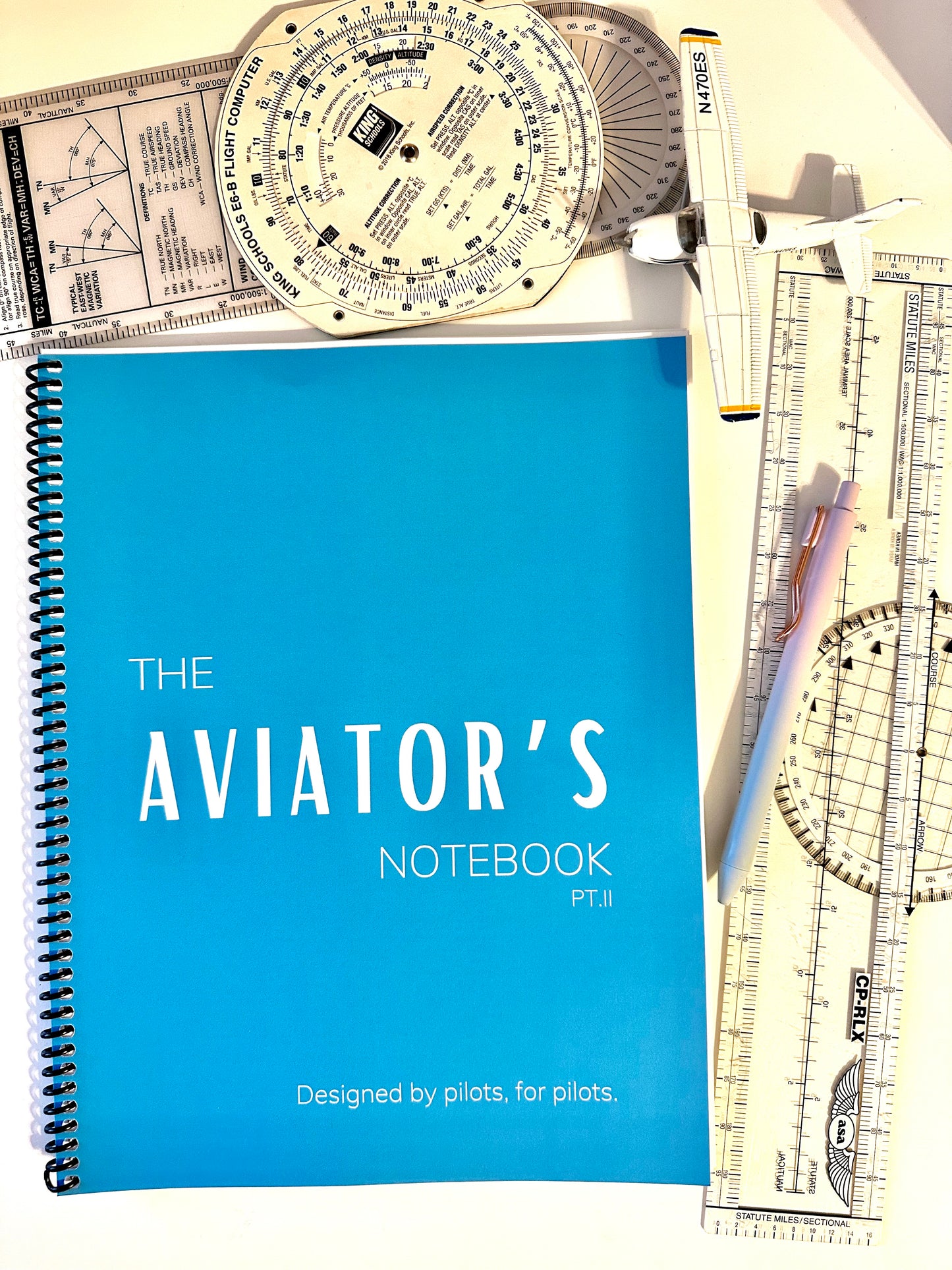 A blue notebook that is called the aviator’s notebook. It has a pen and a small Cessna model. It is a notebook for student pilots in their private pilot flight training. 